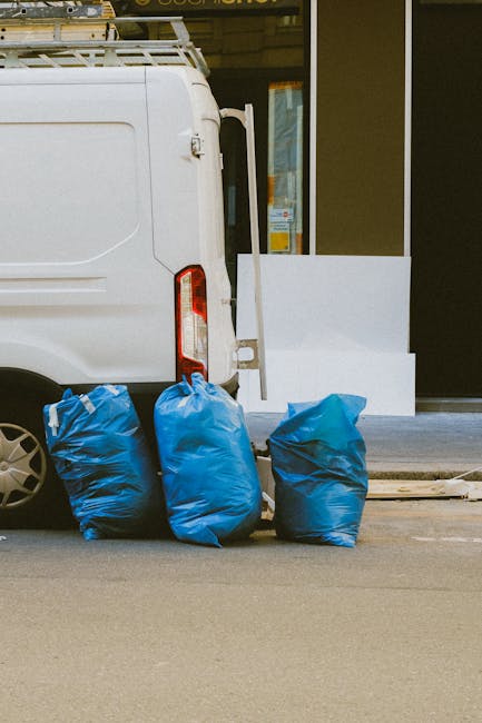 The image shows the rear side of a white commercial van with three large blue plastic rubbish bags placed on the ground directly behind it, likely for collection or disposal. The bags are slightly cru